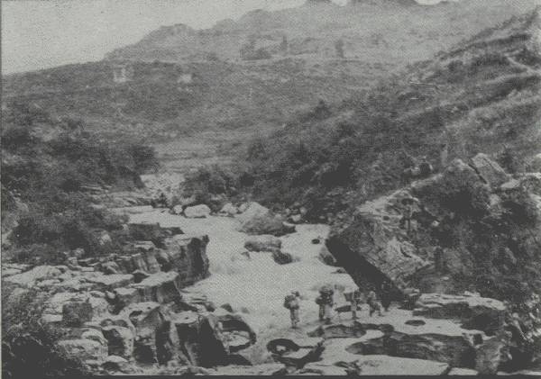 WATCH YOUR STEP

Picture shows nature of main roads in certain sections of western
China; when the rains come, traveling is quite dangerous. Author seen on
boulder at right.